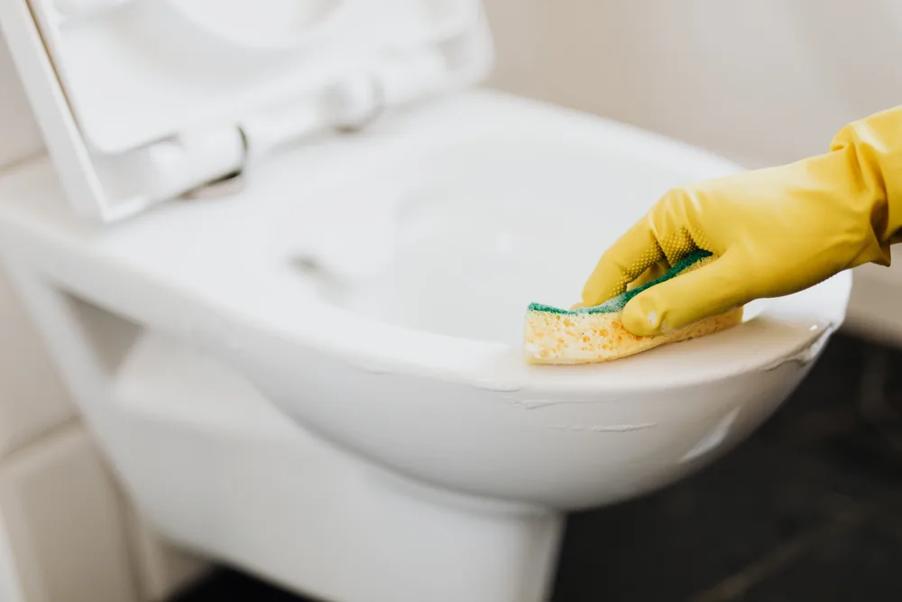 Hand in a yellow rubber glove scrubbing a toilet bowl with a sponge
